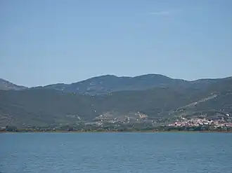 A colour photograph from the middle of a lake of the lake shore with low hills beyond