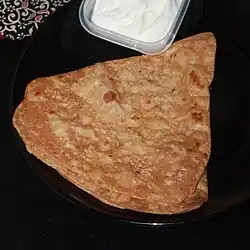 A triangular flatbread that is brown with some darker spots, served next to yoghurt