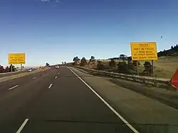 A highway near the top of a ridge. On either side of the highway are big yellow signs reading, "Trucks, Don't be Fooled—4 more miles [6.4&nbsp;km] of steep grades and sharp curves".