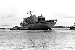 Black and white image depicting a ship being tugged back out to sea.