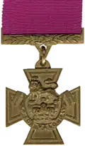 A bronze cross pattée bearing the crown of Saint Edward surmounted by a lion with the inscription 'FOR VALOUR'. A crimson ribbon is attached.