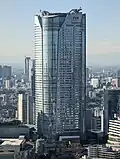 Aerial view of a gray, oval-shaped high-rise lined with rows of windows; the facade is bisected by a smaller midsection