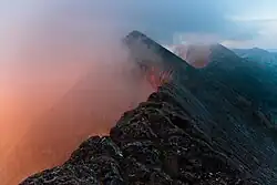 a series of jagged mountain peaks with a pinkish fog rising on the left side