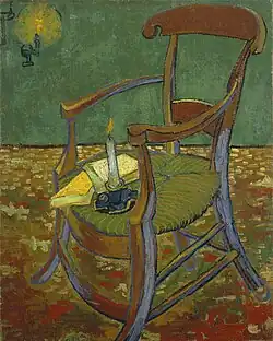 An armchair with a cushion seat; there are two books and a lit candle on the seat. A lit lamp is on the wall.