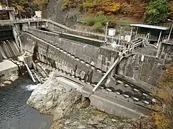 Water is cascading down a series of about 60 concrete steps, built into the side of a sloped concrete wall.