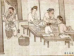 Two women, two men and a child sit at a table, sorting white cocoons in baskets.