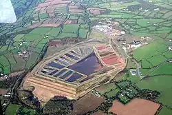 An aerial photo of farmland surrounding a set of about 20 ponds of water, some of them reddish color.