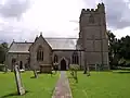 Stone church with square tower. In the foreground are a path and gravestones