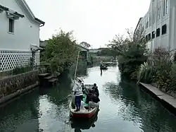 Boats flow down a canal between houses.