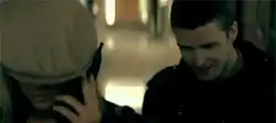 A young man stalking a blonde woman who is wearing a green cap