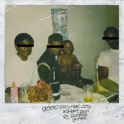 In an instant film photograph, three male adults, with one holding a baby, sitting in a room. The room has a table decorated with glasses, a bottle, and a decorated basket with a poster of a child and a person hanging on the wall. The eyes of the adults are covered with a black bar.