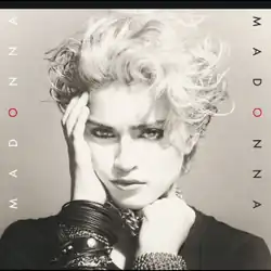 Madonna with her right hand on her cheek and her left hand holding several chains wrapped around her neck.