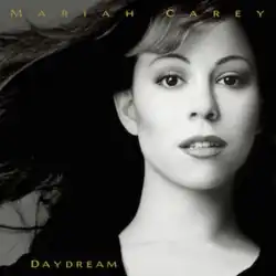 A high-contrast black-and-white close-up of Carey with wind-swept hair fills the frame; her expression is calm and direct as she looks into the camera.