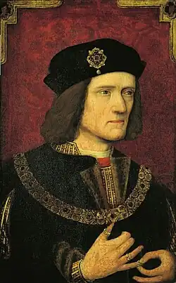 Richard has pale skin, blue eyes, and wears a black hat